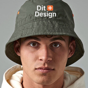 Mand bærer en grøn bøllehat med teksten "Dit Design" foran, iført en beige hættetrøje, stående i et neutralt, gråt rum.