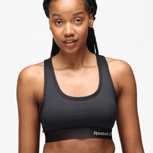 Person iført sort sportstop og leggings står foran en neutral, hvid baggrund. Tekst på tøjet: "Reebok."