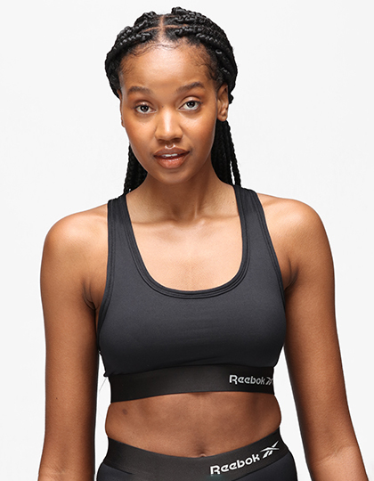 Person iført sort sportstop og leggings står foran en neutral, hvid baggrund. Tekst på tøjet: "Reebok."