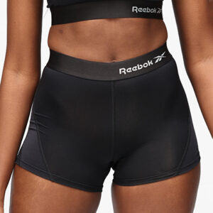 Person iført sorte Reebok shorts står oprejst, med fokus på mave og hofter. Baggrunden er neutral og lys. Tekst: "Reebok" vises på linningen af shortsene.