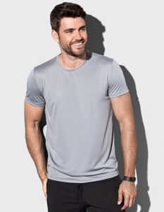 En mand står smilende iført en grå T-shirt. Han holder hænderne ved siden af kroppen. Baggrunden er lys og neutral. Der er ingen tekst i billedet.