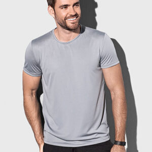 En mand står smilende iført en grå T-shirt. Han holder hænderne ved siden af kroppen. Baggrunden er lys og neutral. Der er ingen tekst i billedet.