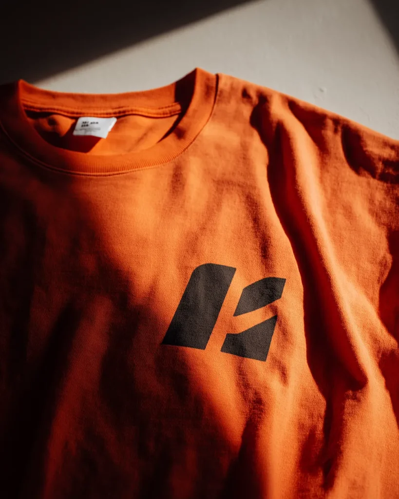 Orange t-shirt med sort logo tryk i nærbillede